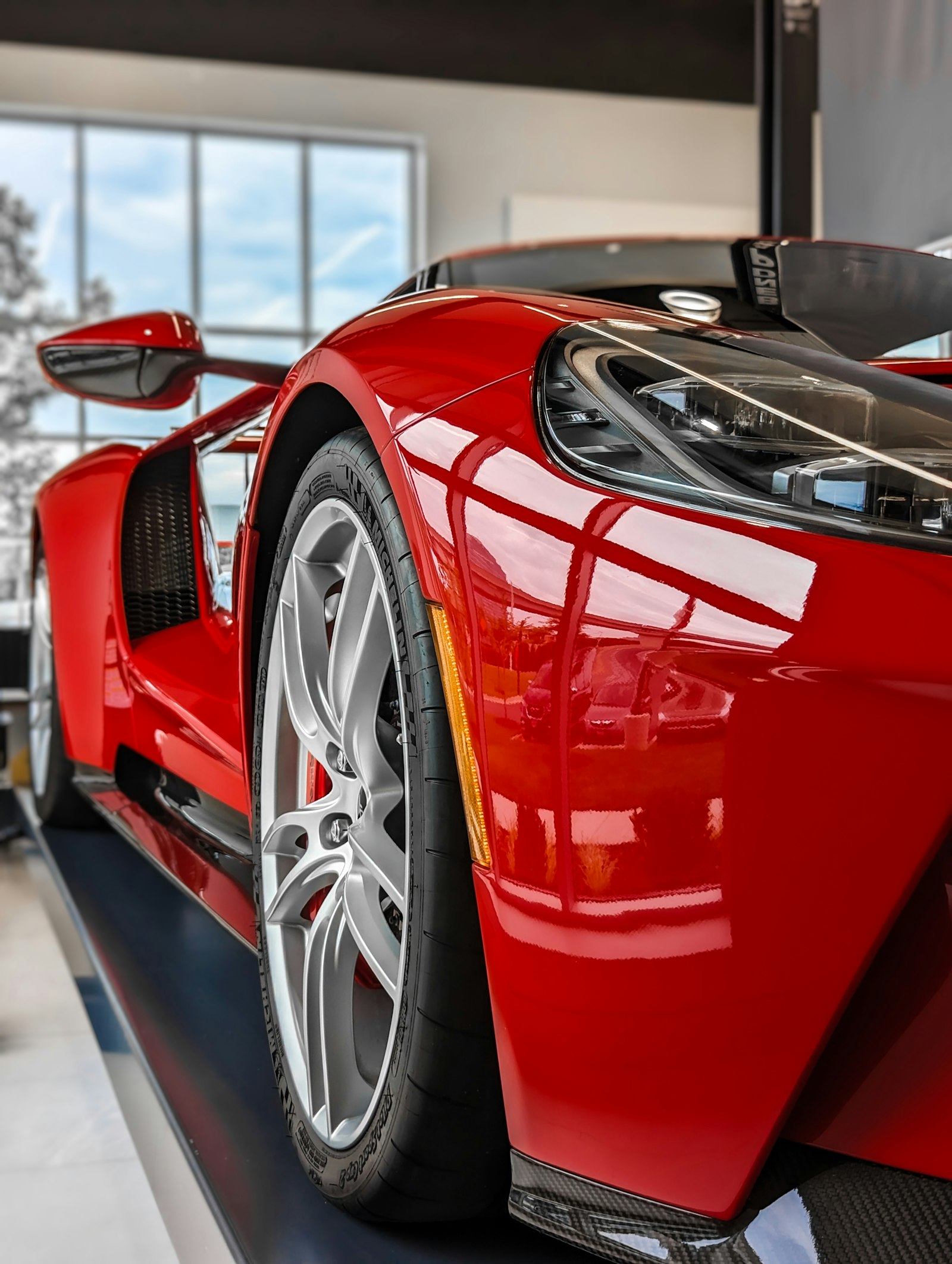 Front-three-quarter close-up of a red Ford GT in a clean showroom bay, with daylight from a tall window behind